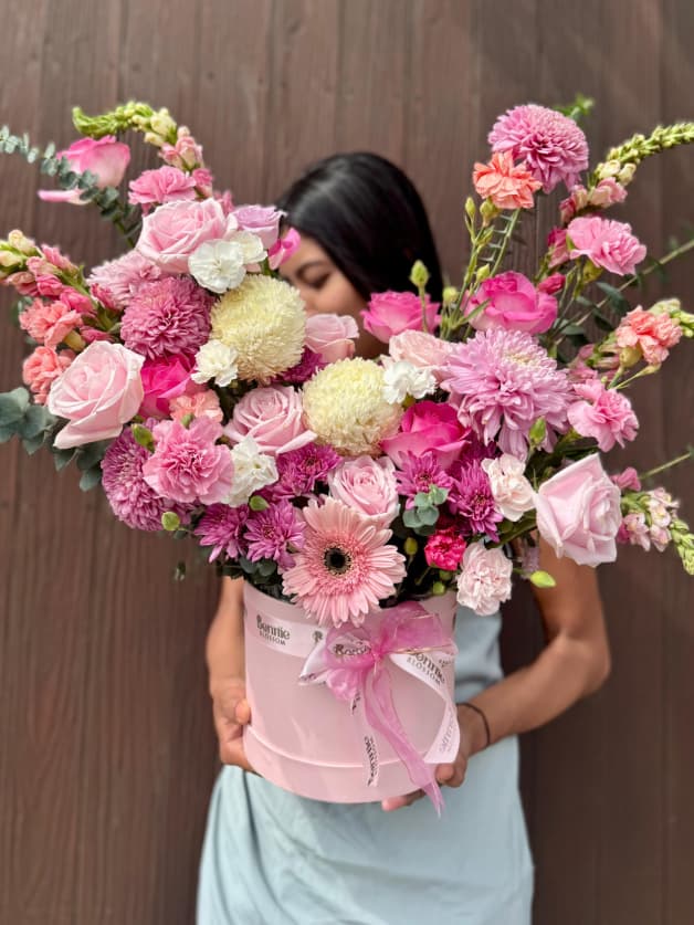 A luxurious large pink box overflowing with pink roses, carnations, and snapdragons